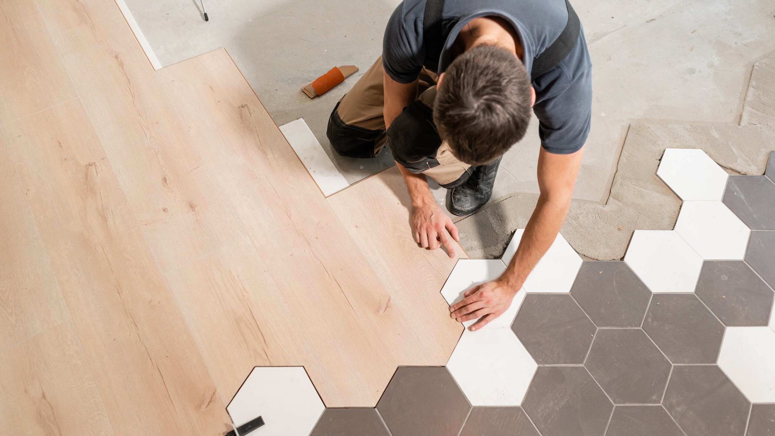 gallery-04 A person installing a new floor, placing a gray hexagonal tile next to other gray, white, and wood-like tiles.